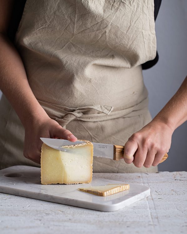 mujer cortando queso de oveja con cuchillo mango d eolivo sobre tabla de marmol blanco