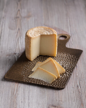 Queso de Oveja de Leche Cruda sobre tabla de Cerámica artesanal en tonos oscuros.