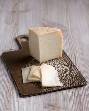 Queso de Cabra Payoya semicurado en pieza sobre tabla ceramica oscura. Se muestra el corte.