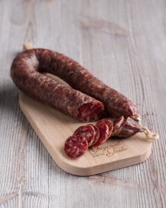 Salchichon Embutido de León de herradura presentado en pieza y con algunos trozos sobre tabla de madera